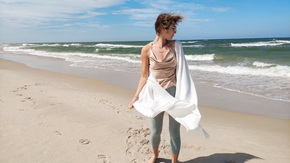 A woman stands on Łeba Beach in Poland, with waves and a clear blue sky.